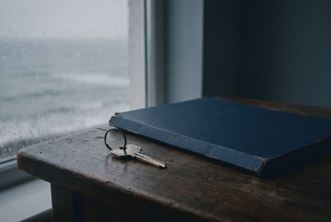 A key on a ring beside a closed navy folder on a wooden sill, with rain on the window behind